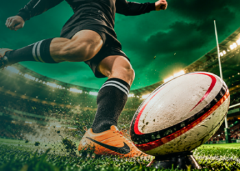 Rugby players dressed in black kicking the rugby ball inside the rugby stadium.